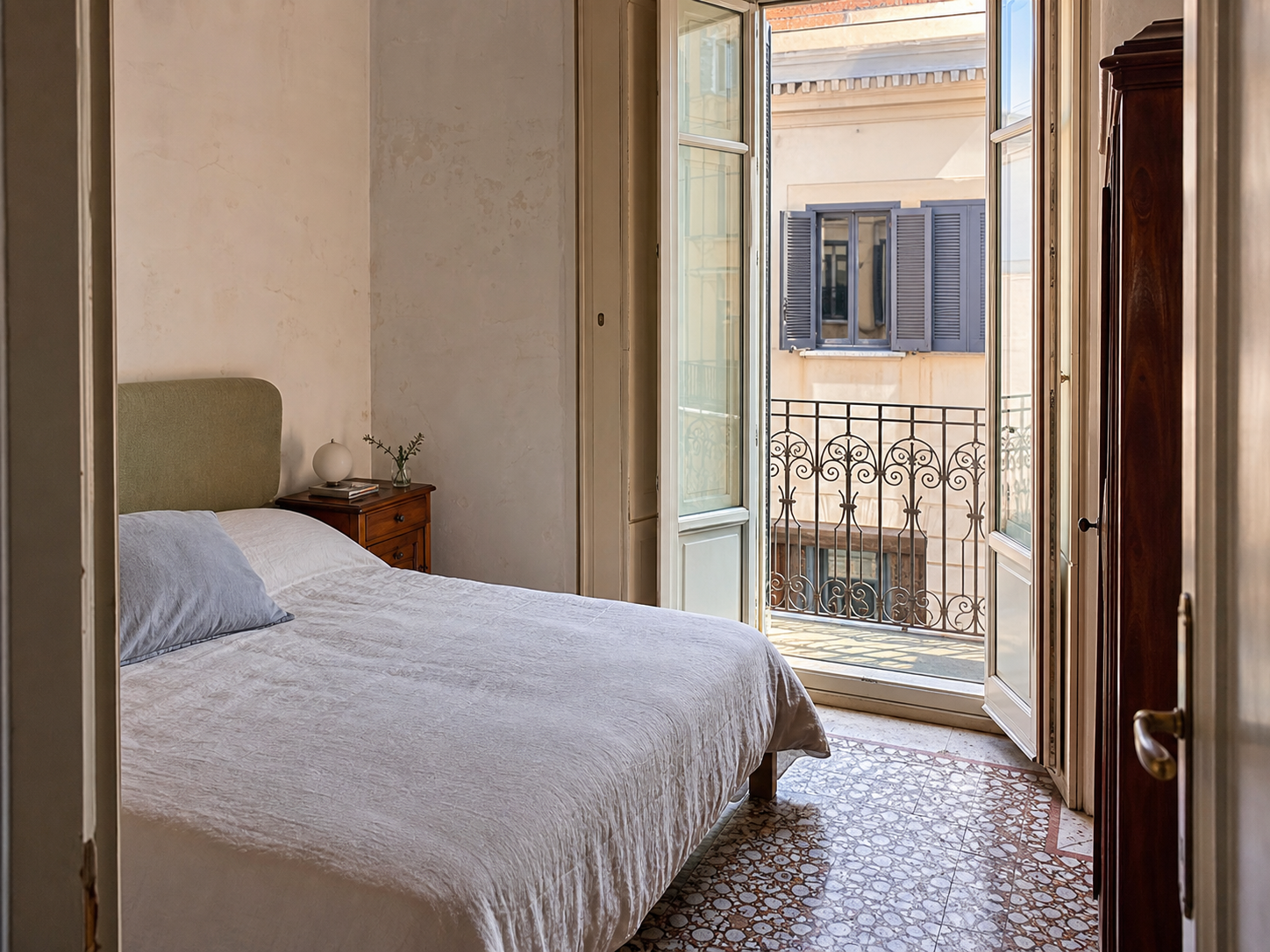 Camera di un appartamento italiano con letto in lino e balcone affacciato sui palazzi vicini