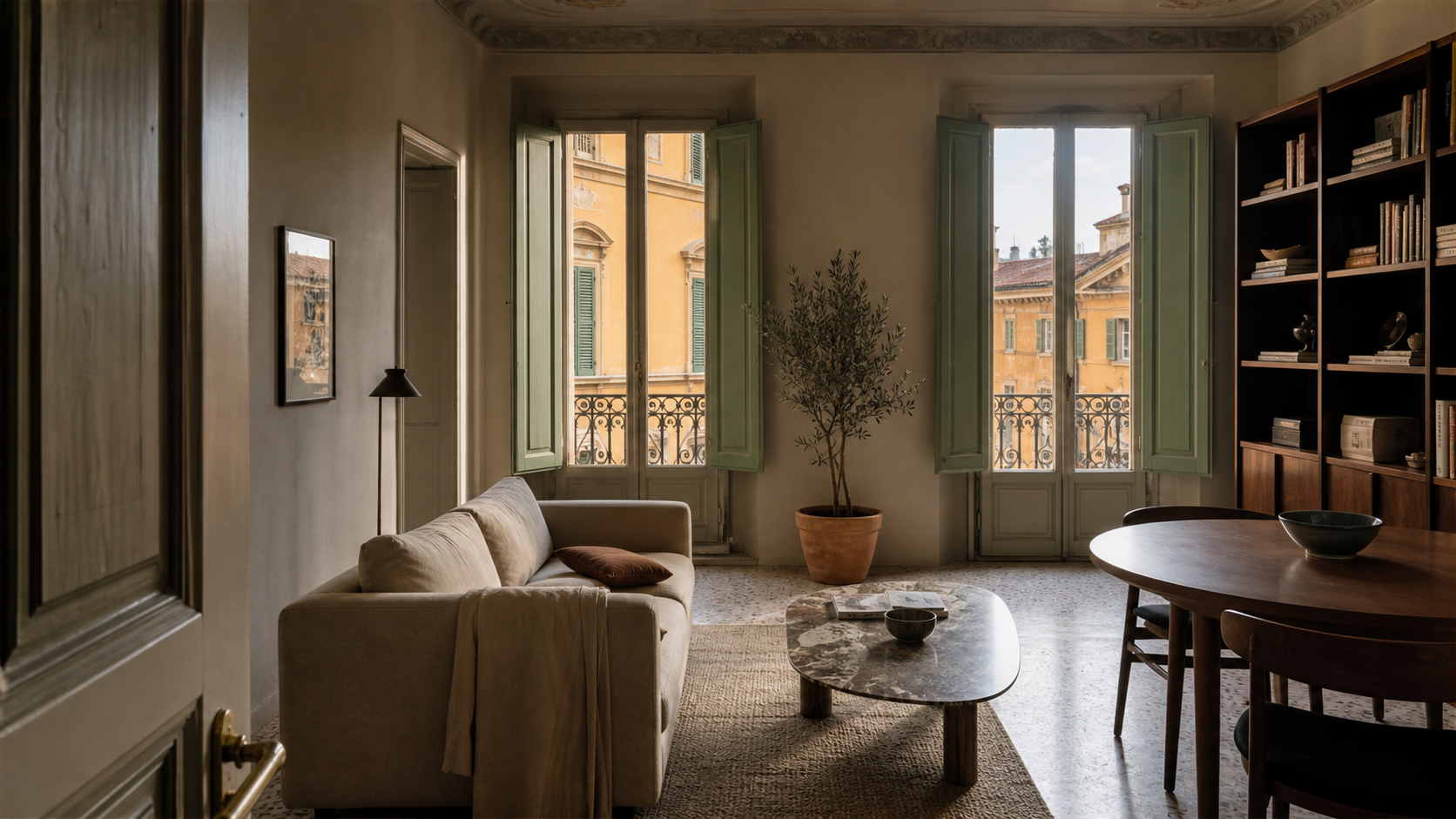 Soggiorno di un appartamento italiano in palazzo storico, con persiane verdi aperte su una facciata color ocra